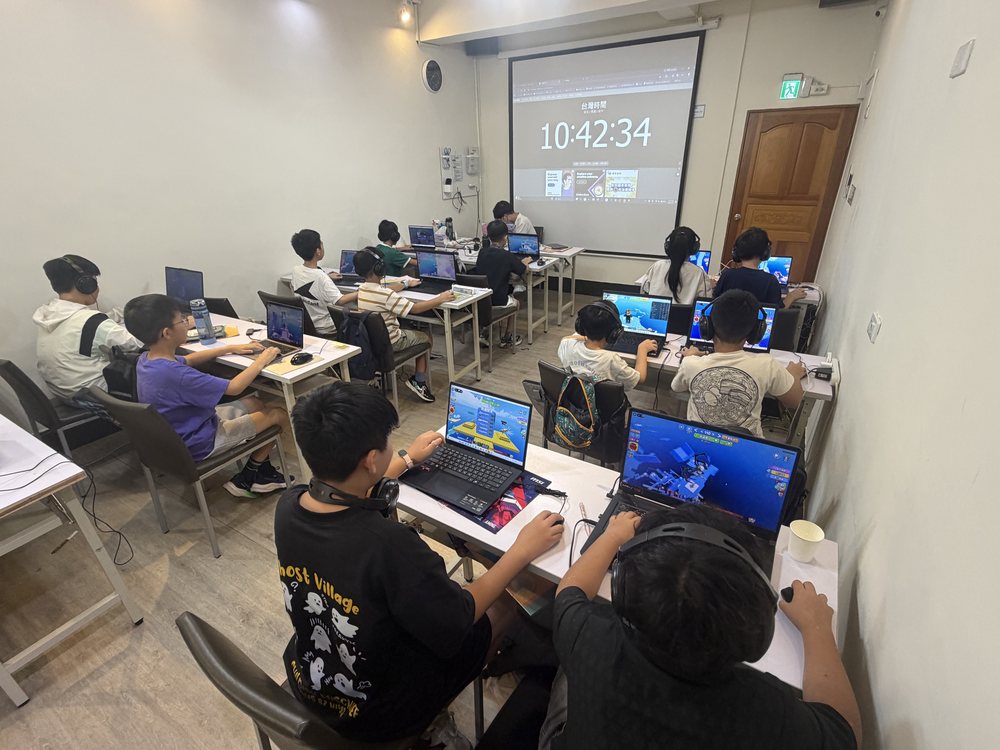 台中南屯教室上課實景，整班學生各自使用筆電與耳機操作程式，教室前方設有投影幕