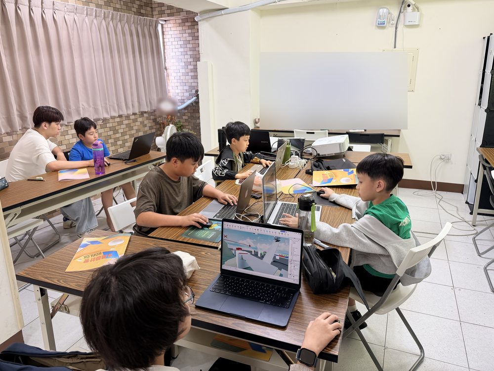 台南東寧教室的 Roblox 遊戲設計營課堂,學生圍坐長桌各自用筆電製作遊戲,老師在後方陪同操作