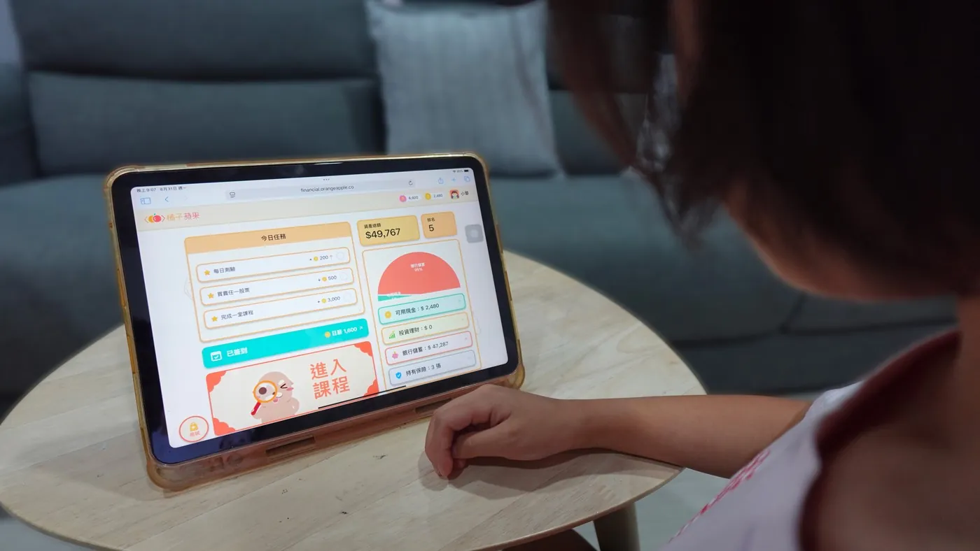 孩子在家中以平板使用財商學習平台，畫面顯示今日任務、每日簽到、資產總額與資產配置環圈
